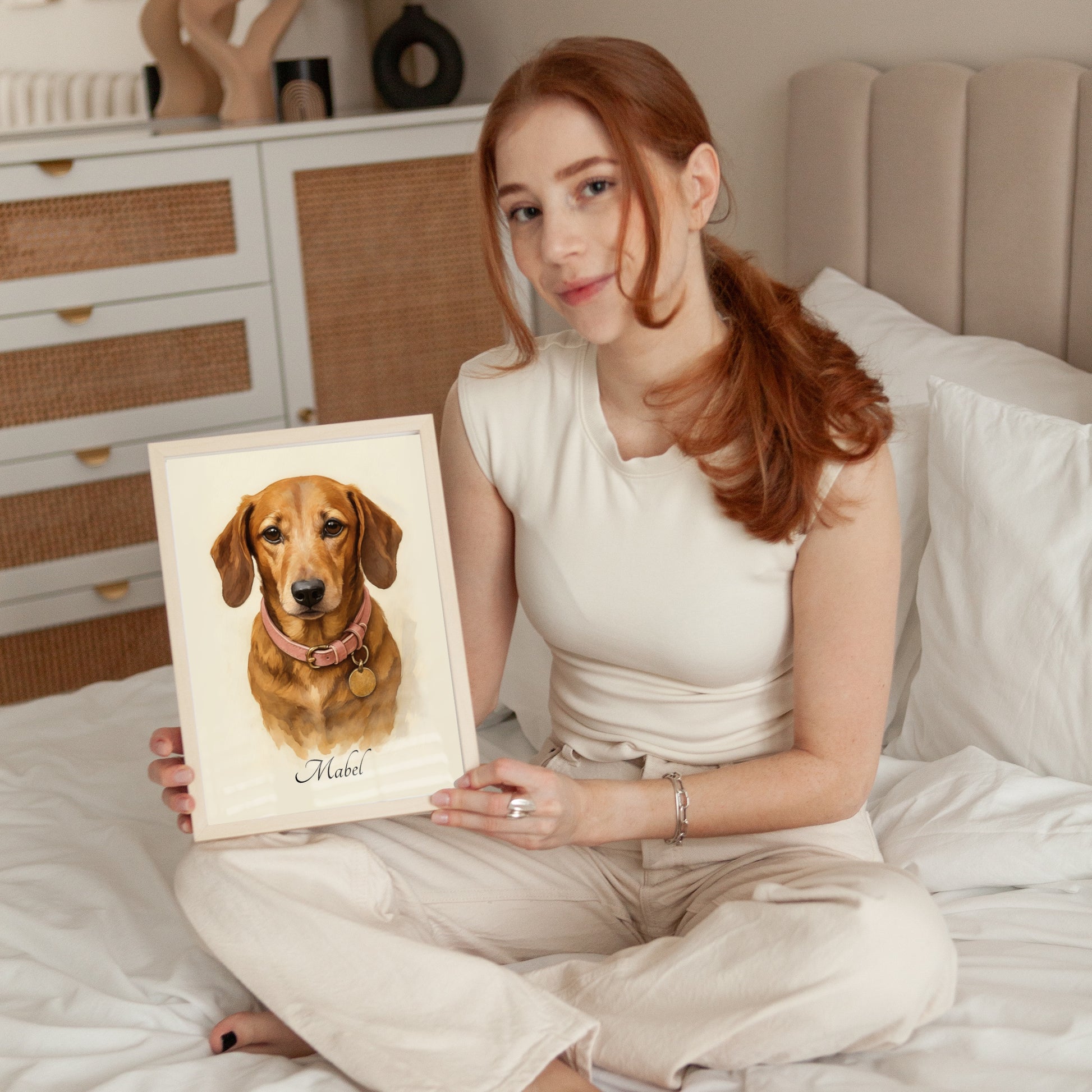 Woman holding a framed portrait of a dog on a bed
